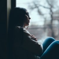 Silhouette of a woman leaning against a window looking outside and looking sad.