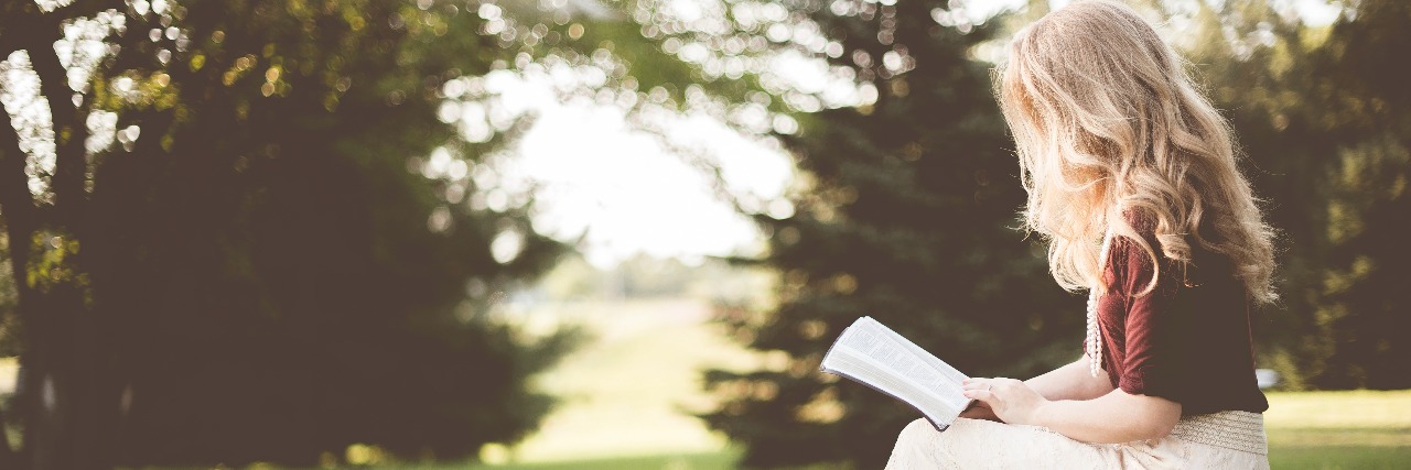 woman in white skirt reading book in field