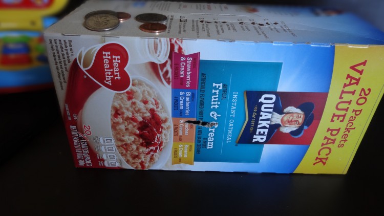 Quaker oatmeal box laying on its side with slits and coins on the top