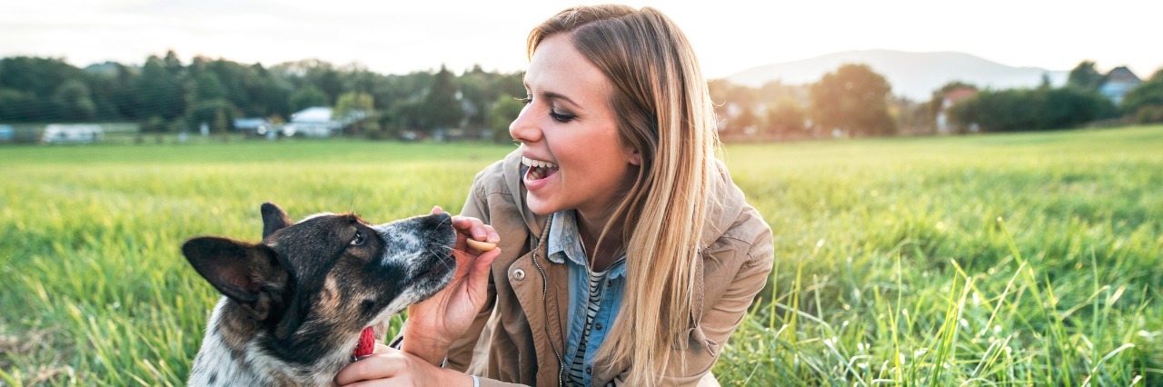 Why I Decided to Wear a Medical Bracelet Because of My Epilepsy Woman with dog, she is kneeling down, smiling at her dog and giving him a treat