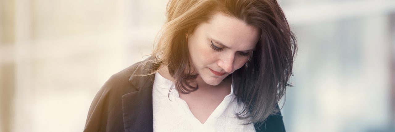 What Has Helped Me Cope With Grief as a Bereaved Parent Woman wearing a white shirt and blue sweater looking down, she seems sad
