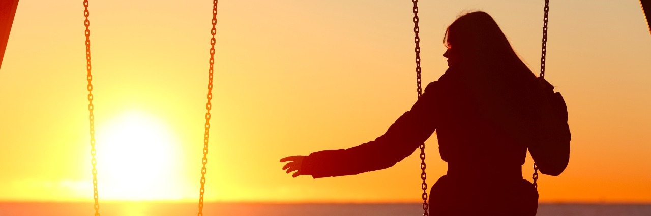 Silhouette of a woman alone on a swing, reaching out to an empty swing
