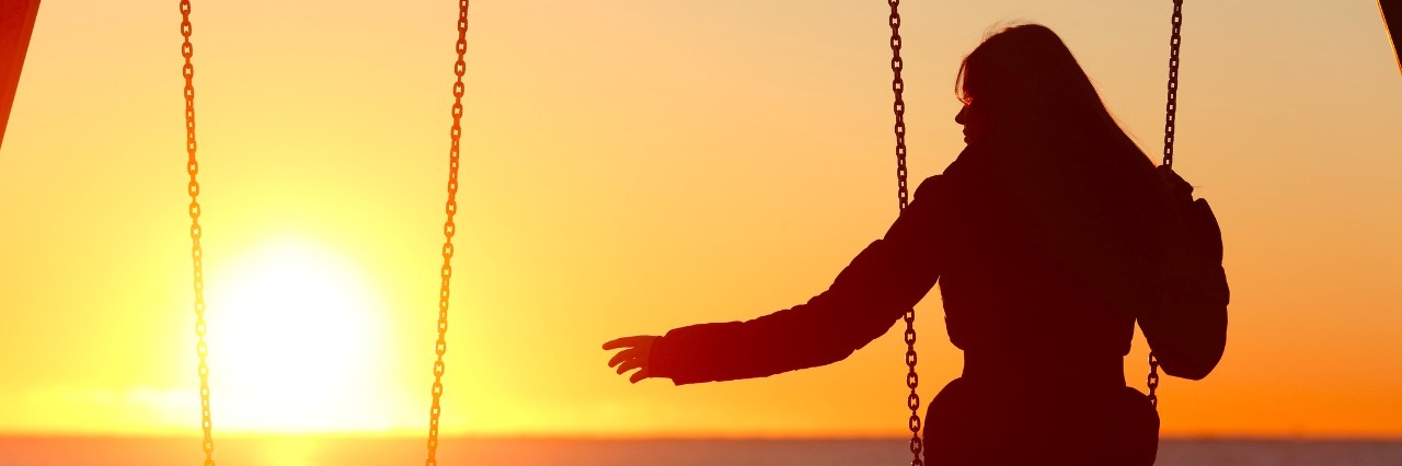 How Grief Affected My Physical Health After My Dad's Passing Silhouette of a woman alone on a swing, reaching out to an empty swing