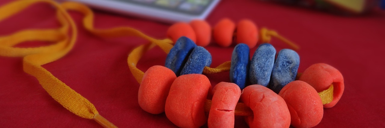 Beads made out red and blue play-doh stringed with a yellow shoe lace