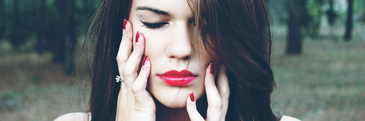 Woman wearing red lipstick with eyes closed and hands on face