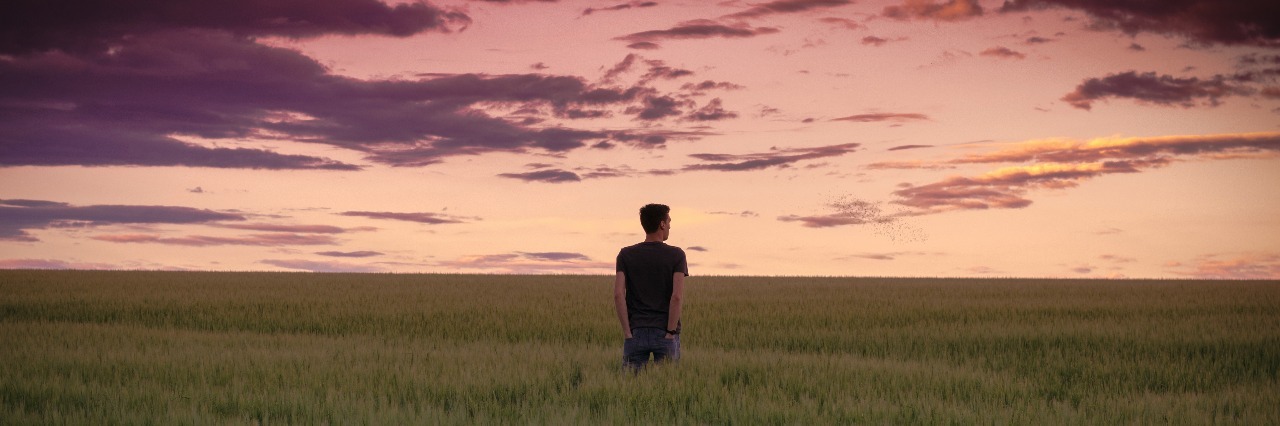 man standing alone in field at sunset