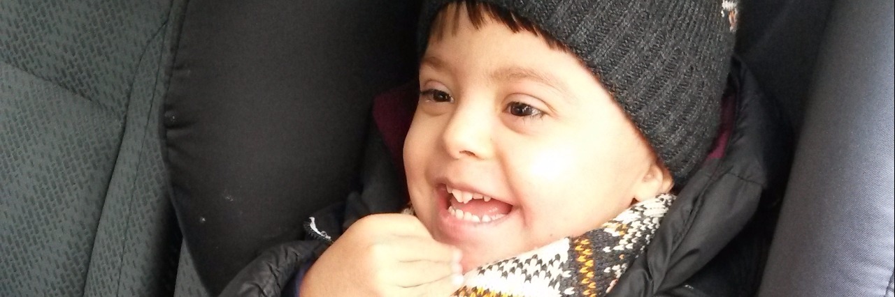 Boy in car seat in car, wearing beanie and laughing