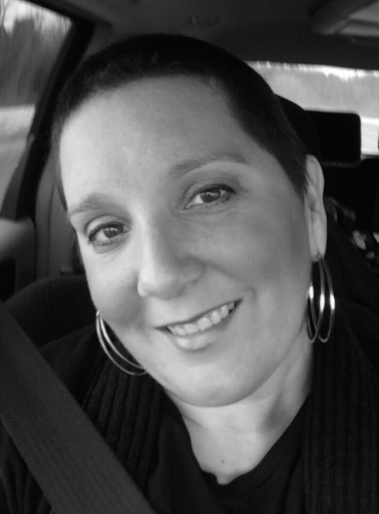 Woman sitting in car with seatbelt on, smiling and looking at camera