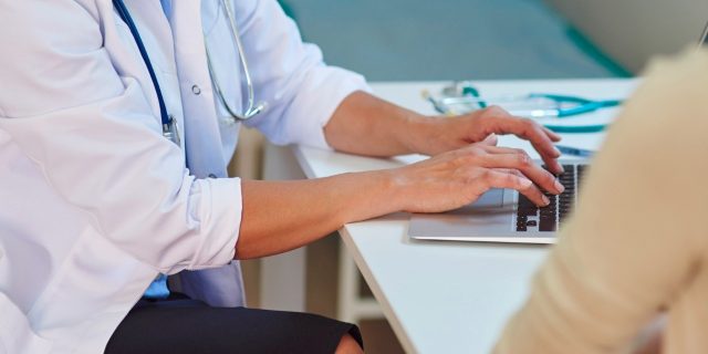 Patient having a conversation with doctor as doctor types on laptop