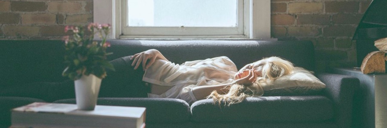 Signs of Having Crohn's Disease blonde woman laying on couch next to a window and vase of flowers