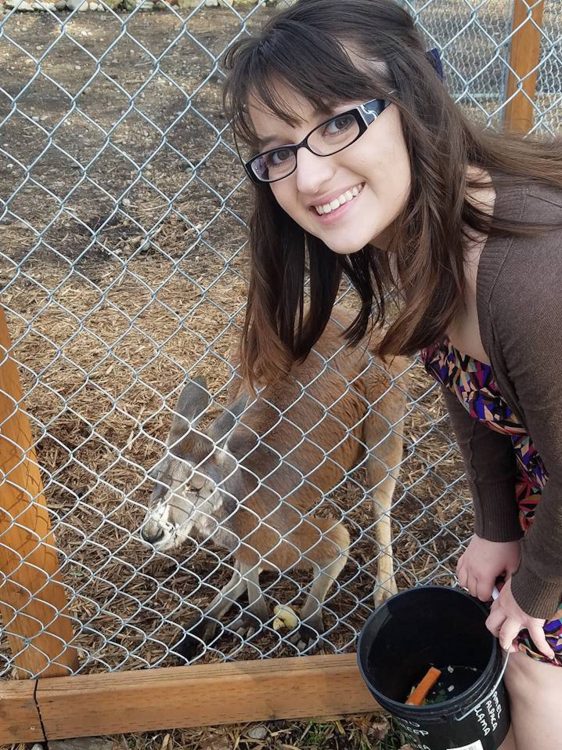 woman bending down next to kangaroo behind a fence