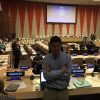 Tom at World Autism Awareness Day 2017 at the United Nations, standing in front of tables with microphones and the stage in the background