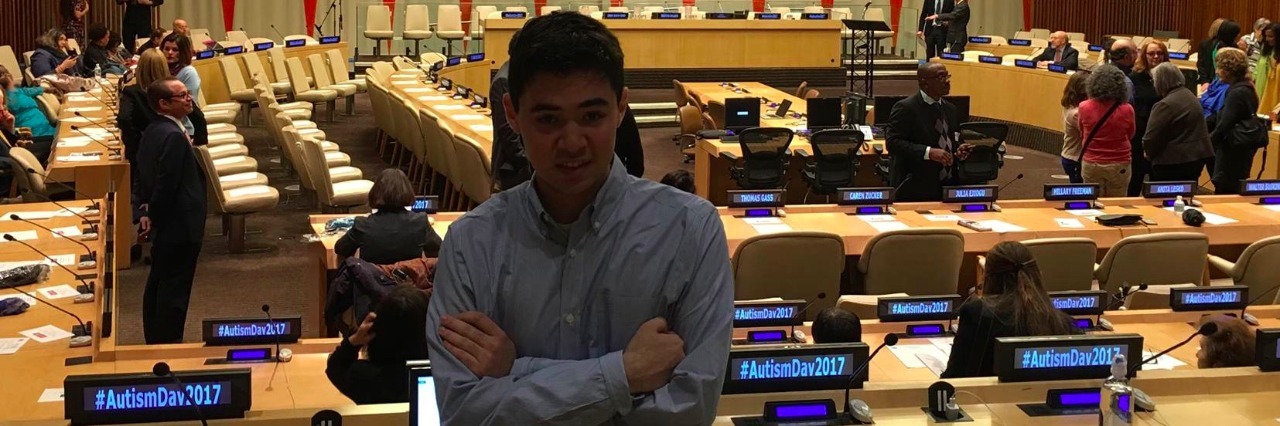 Attending World Autism Awareness Day at the United Nations as a Young Person With Autism Tom at World Autism Awareness Day 2017 at the United Nations, standing in front of tables with microphones and the stage in the background