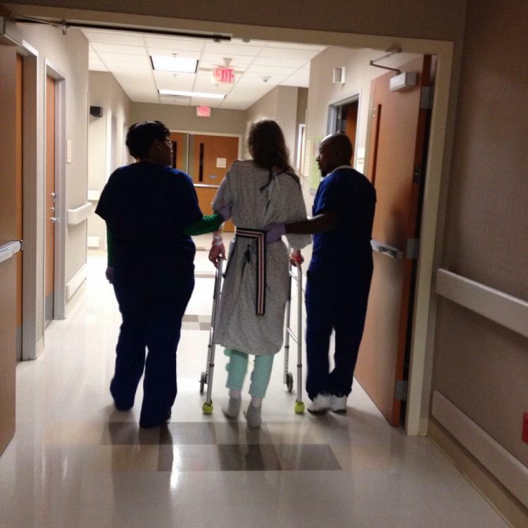woman in hospital walking with walker and nurses on each side