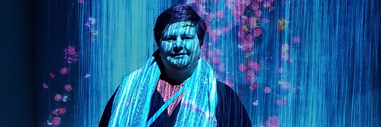 Being Disbelieved With Hypermobile Ehlers-Danlos Syndrome woman standing in a room with blue and pink lights