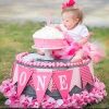 Little girl with down syndrome sitting on top of ink decorated stand and a pink birthday cake, she is reaching for the frosting