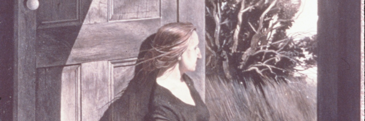 Portrait of a woman leaning against a large wooden door looking into the outdoors