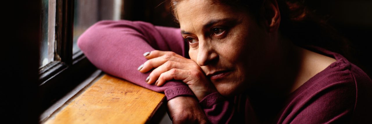 The Hole in Hopelessness After My Son's Death Woman wearing a long sleeve purple shirt looking outside a window, she is sad