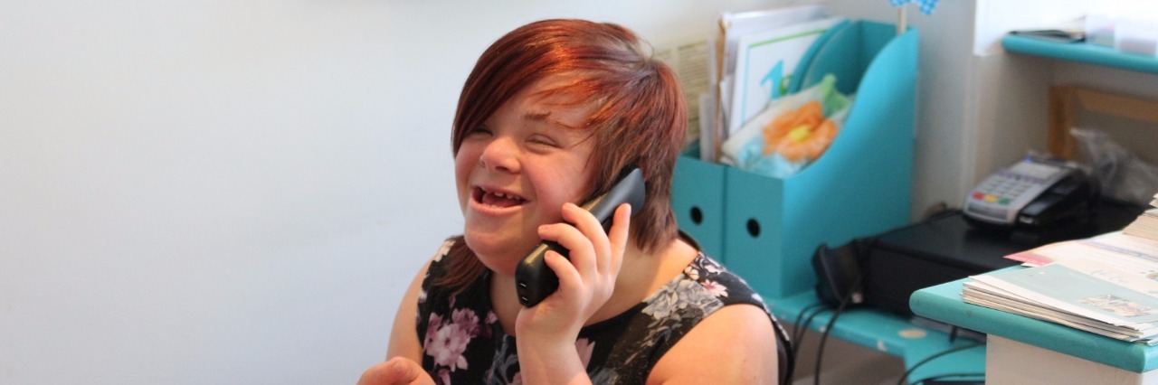 Speaking Up About Prenatal Testing as Someone With Down Syndrome Heidi Crowter, a woman with Down syndrome, sitting ona chair, smiling, and talking on the phone
