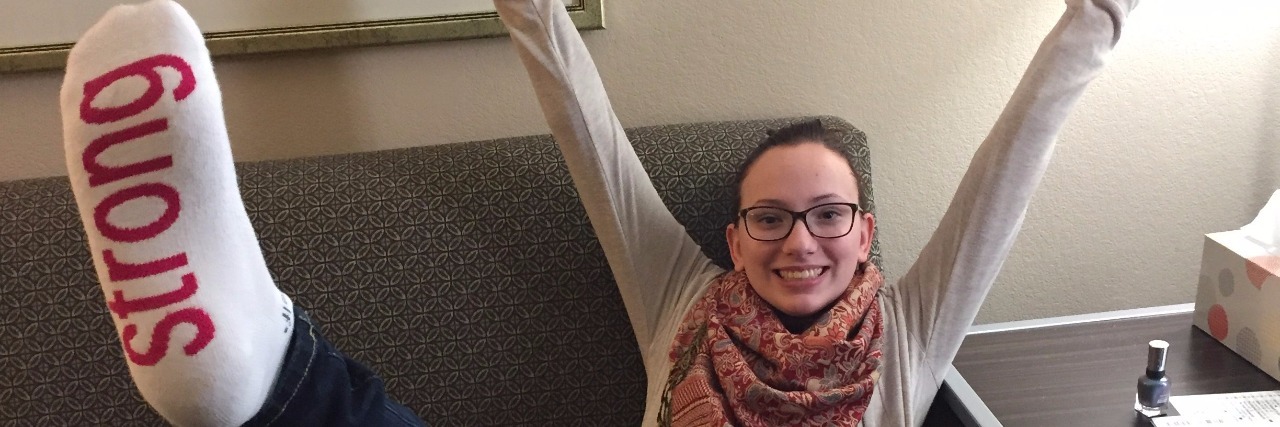 A Survival Guide for the Difficult Days, From a Chronic Pain Warrior Woman sitting with her arms up in the air, smiling.