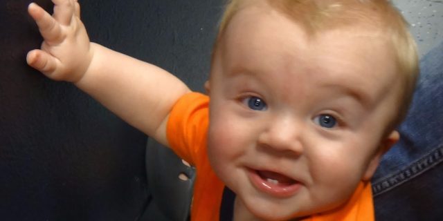 Baby with one hand raised, wearing an orange shirt