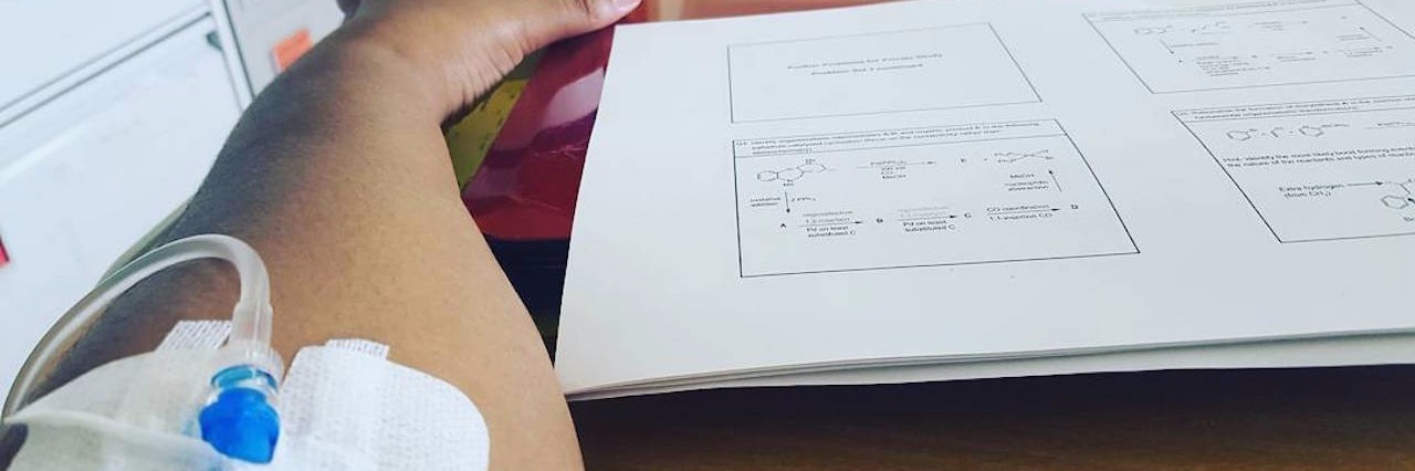 Lupus: Learning to Accept Your Limitations With Chronic Illness woman's arm with an IV in. she's holding a mug of coffee and studying for school