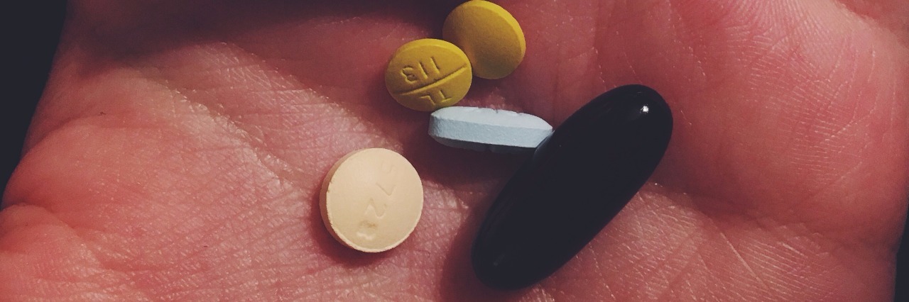 The Phrase I Get Tired of Hearing About My Chronic Illness Woman holds handful of medication in her hand.