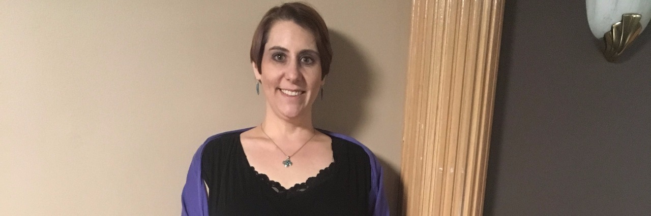 Why I Love the Braces I Wear Due to Ehlers-Danlos Syndrome woman standing next to wall showing brace on ankle, wearing black dress