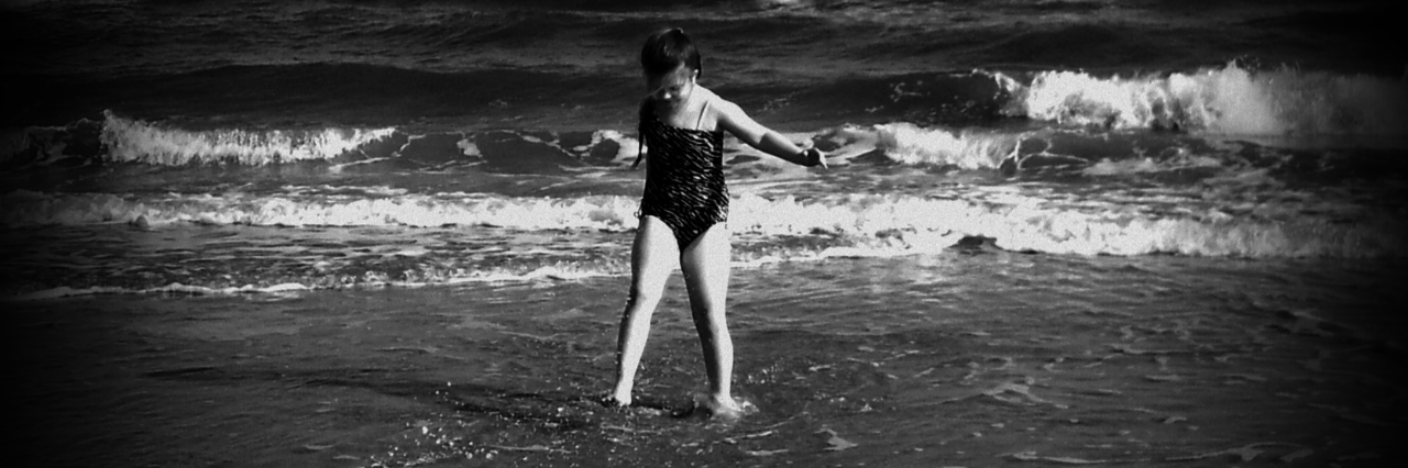 black and white photo of young girl walking along the beach