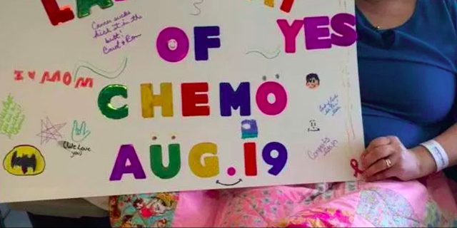 Woman holding decorated sign that says last day of chemo aug 19