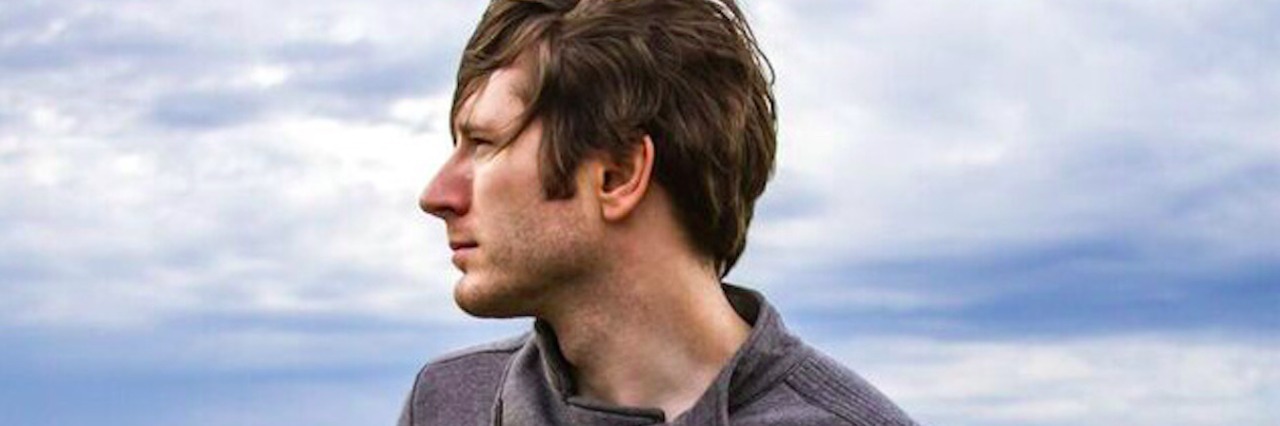 How Owl City's Music Helps Me Through Sensory Overload Profile of man standing in front of a grass and tree landscape, with cloudy sky