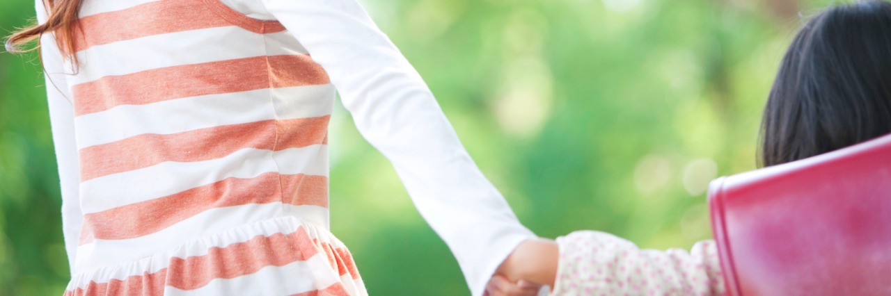 My Daily Mantra After My Child’s Sensory Processing Disorder Diagnosis Woman holding daughter's hand, smiling, outdoors near trees