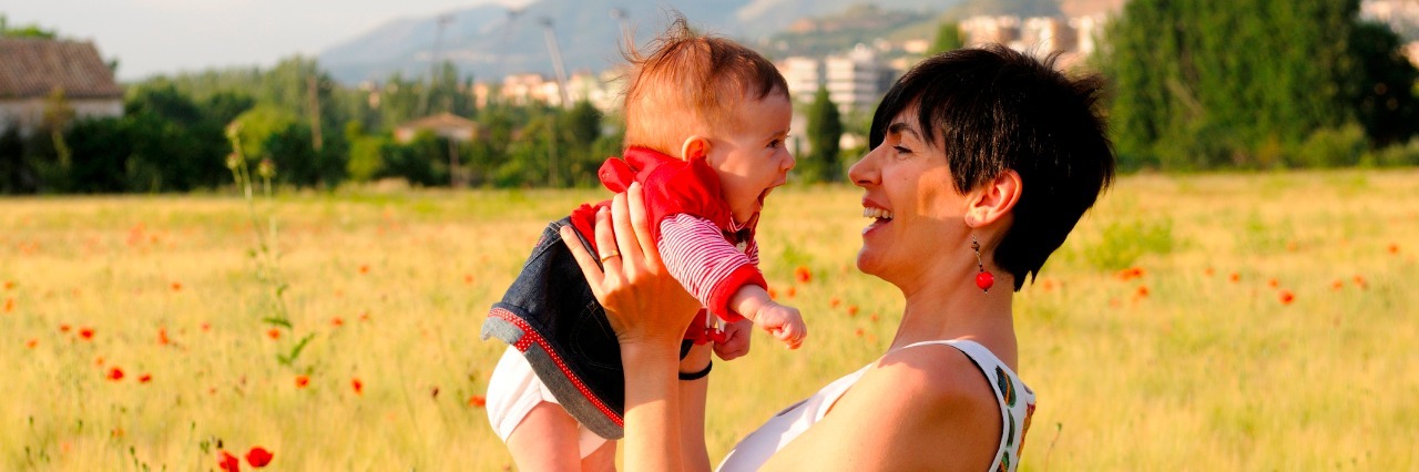 Apert Syndrome and the Benefits of a Diagnostic Label Woman smiling in a poppy field with her baby girl.