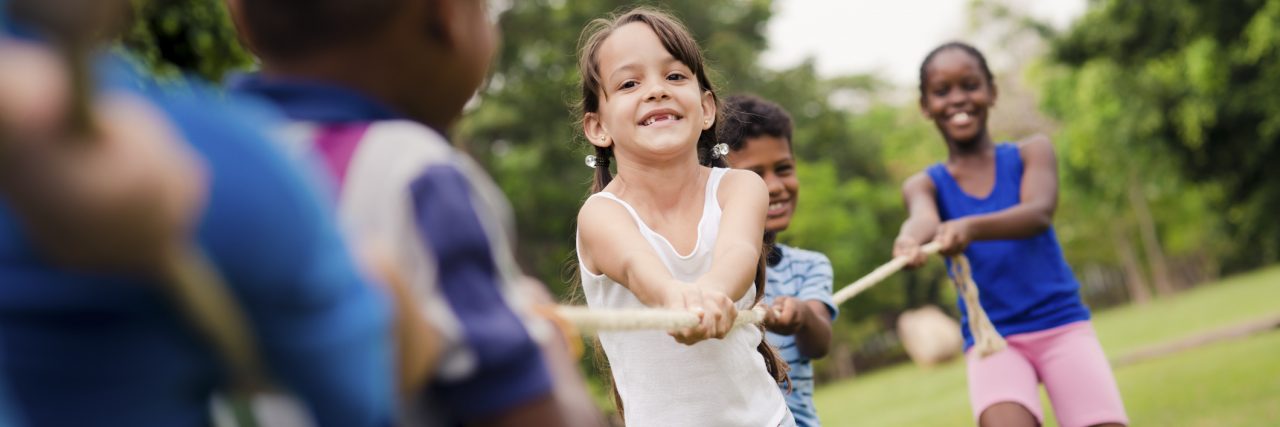 school children playing tug of war with rope in park