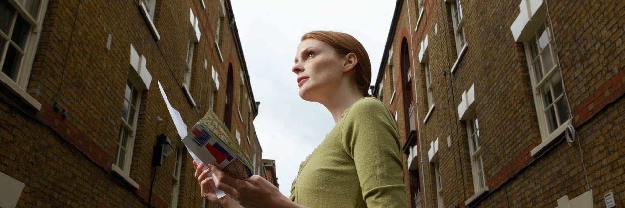 Accepting and Adapting to Life With Chronic Illness woman holding a map and standing between two brick buildings on the street