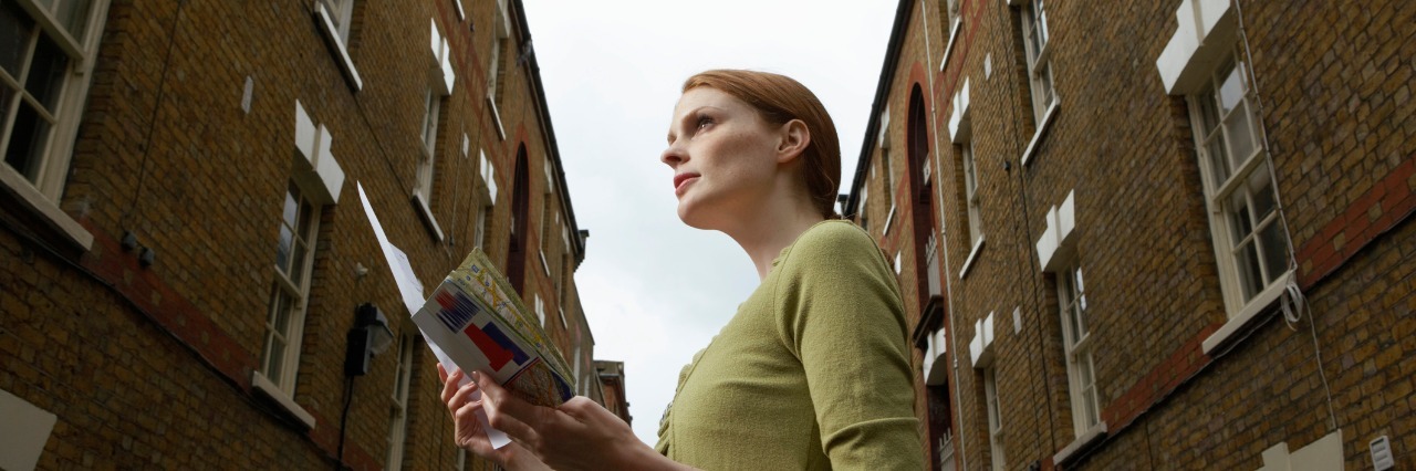 woman holding a map and standing between two brick buildings on the street