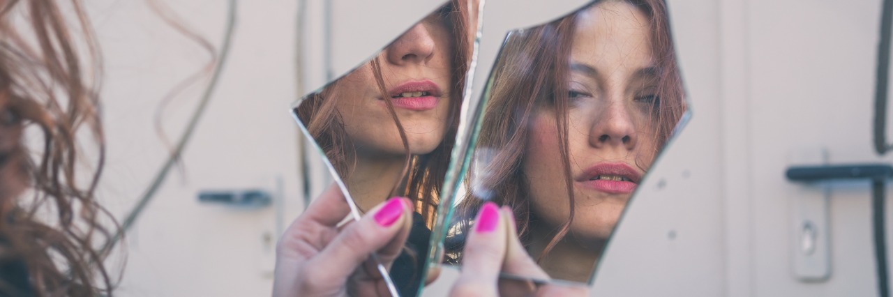 woman looking at her reflection in broken mirror pieces
