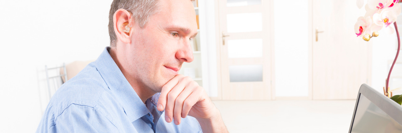 Choosing a Career With Hearing Loss Man with hearing aid working with laptop and mobile phone.