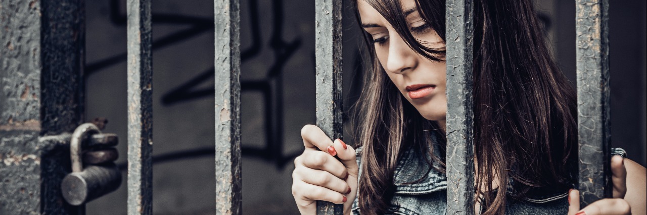 young woman trapped behind metal bars imprisoned