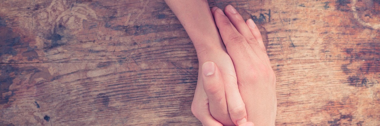 Focusing on Helping Others Helps My Anxiety Close up on a man and a woman holding hands at a wooden table