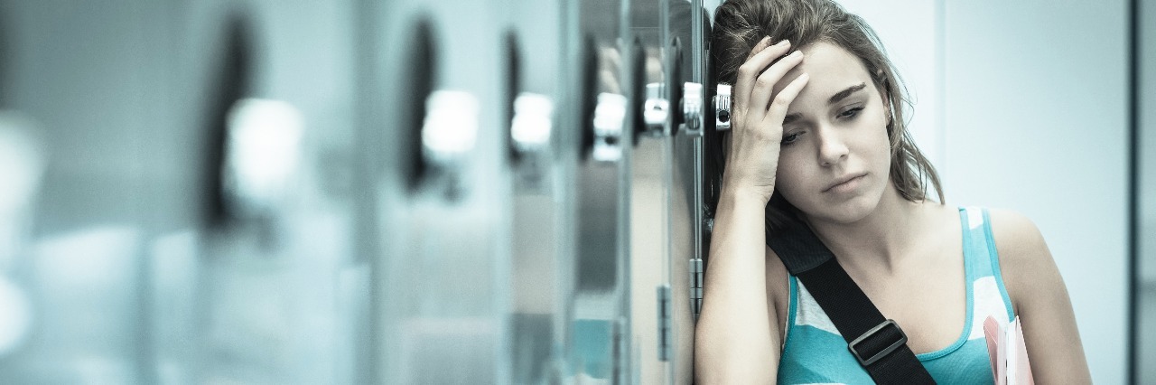 Why High School Mental Health Education Is So Important sad female student wincing and leaning against locker