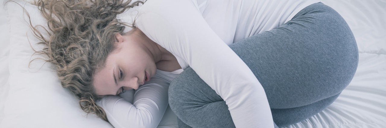 depression concept of young woman with blonde hair curled up in bed hugging knees