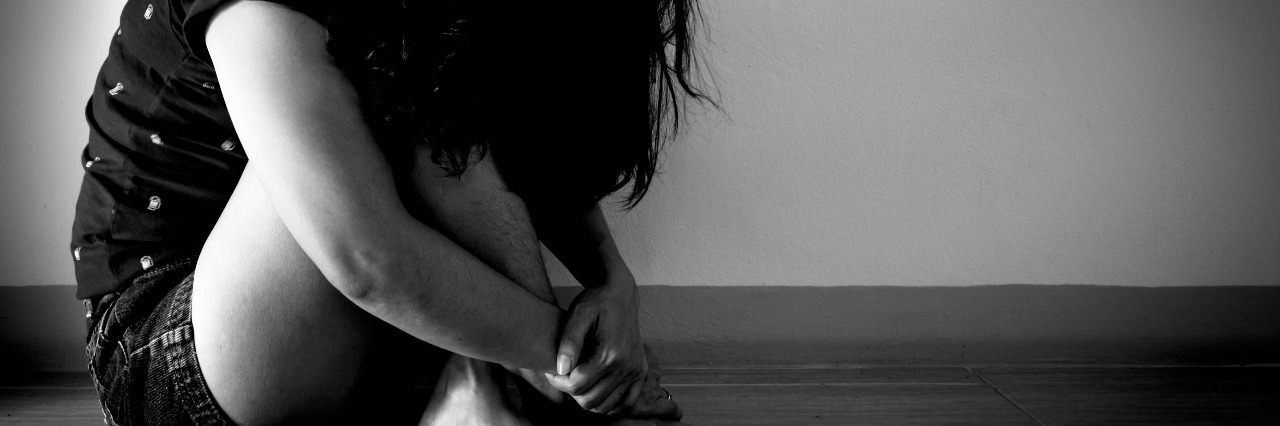 black and white photo of woman hugging knees with face covered by hair