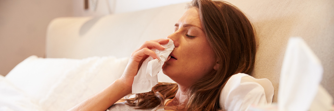 Woman in bed with a cold blowing her nose.