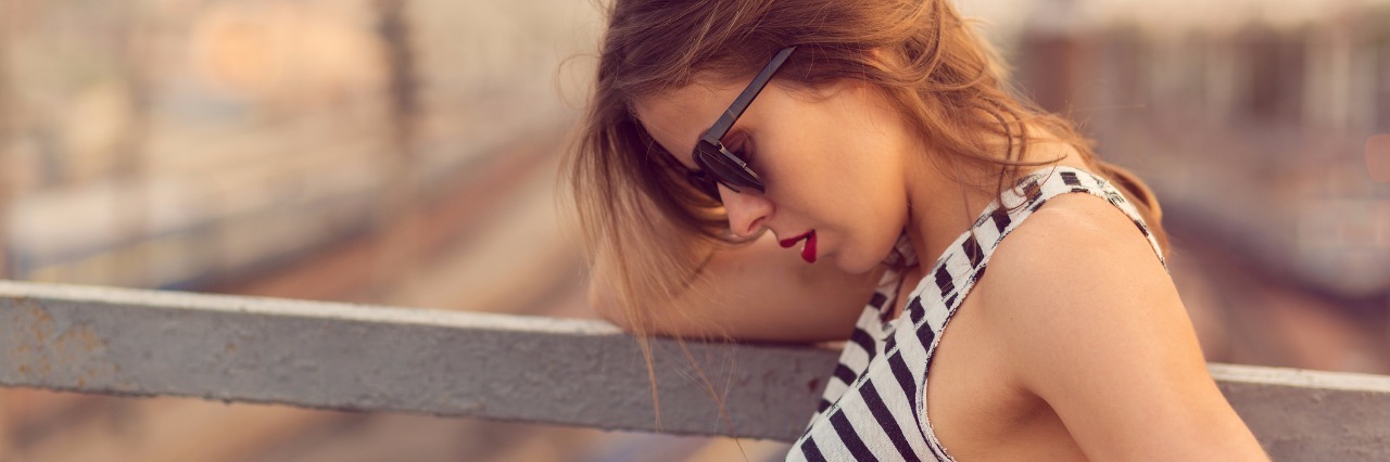 Ehlers-Danlos, Fibromyalgia: Telling Sick People They Look Healthy woman in striped dress and sunglasses standing on a bridge and looking down at her feet