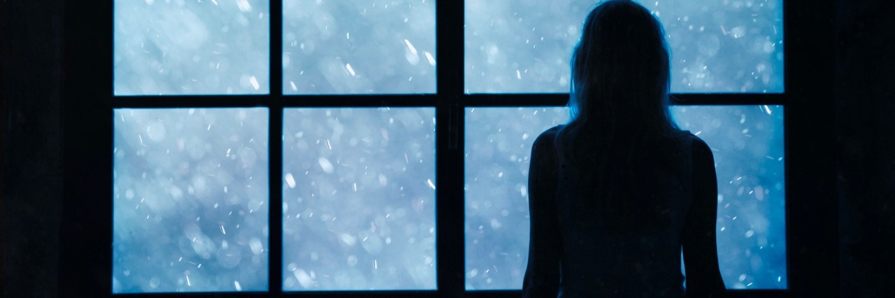 silhouette of woman looking through window at snow