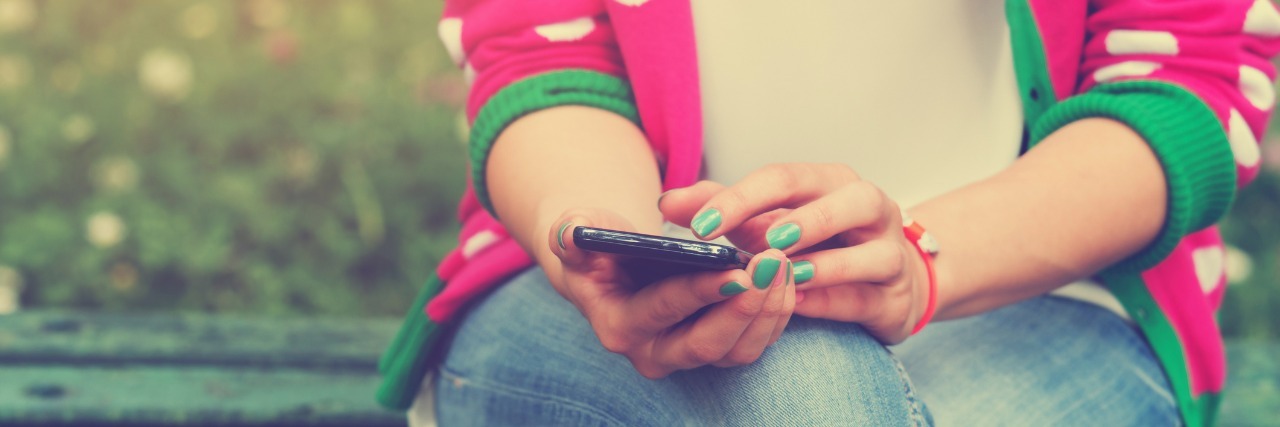 How a Text From a Friend Helped Ease the Guilt of Fibromyalgia Woman texting outside on a bench.