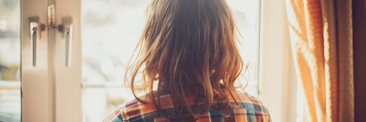 Grieving Loss and Finding Joy After a Chronic Illness Diagnosis Young woman is standing and looking out the window