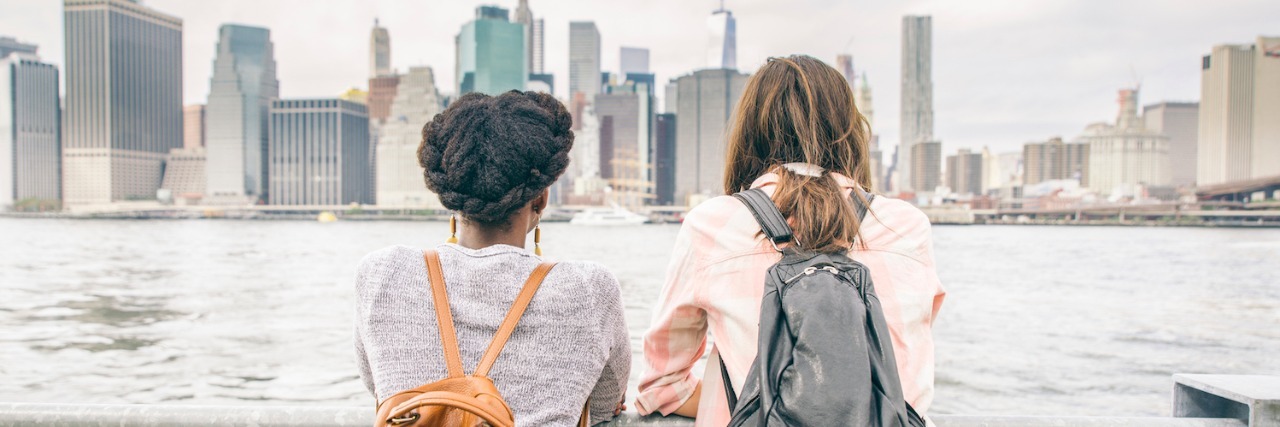 Two women leaning on railing, looking at city skyline and water