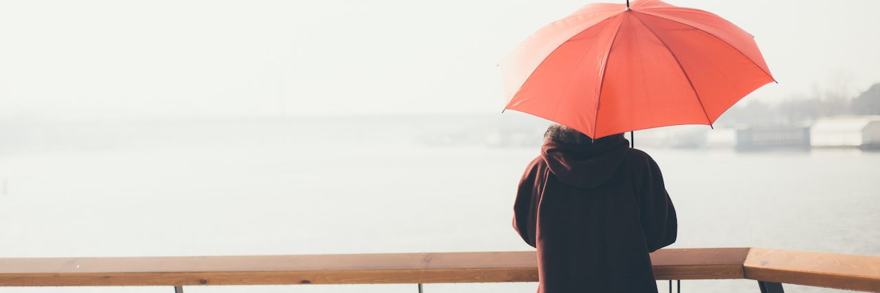 How Cognitive Behavioral Therapy Helps Me Manage Bipolar Disorder Woman standing at the balcony looking at the river and holding umbrella